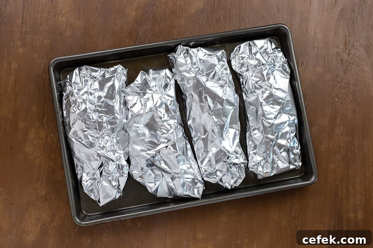 Four foil wrapped chicken breasts on baking pan.