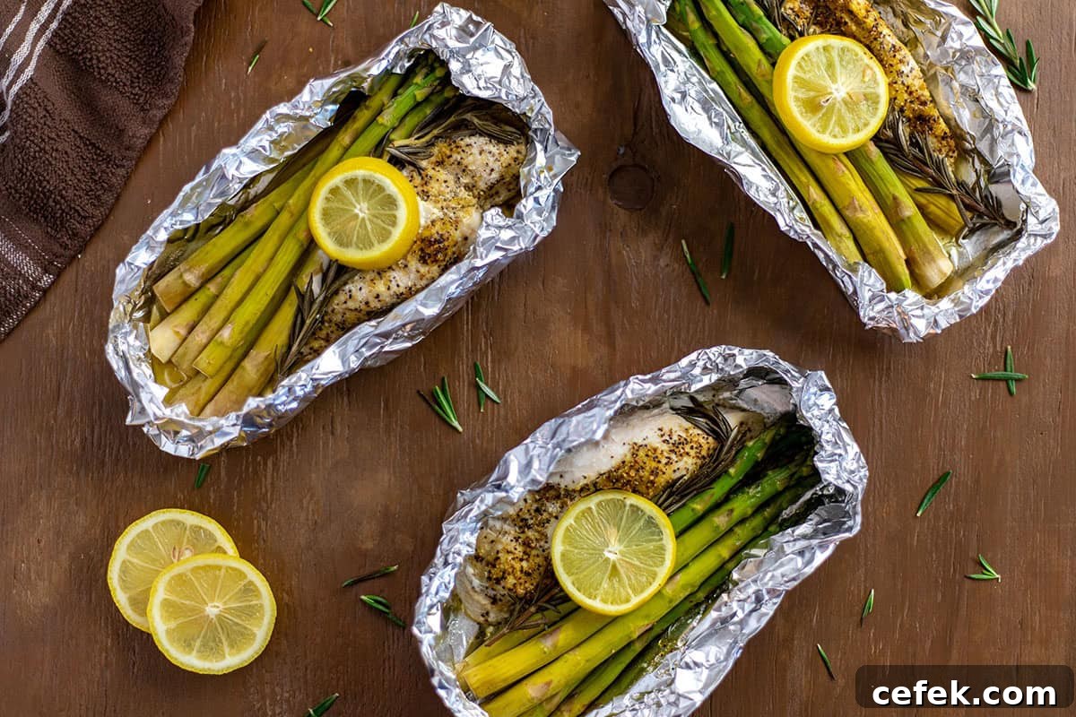 Three Lemon Pepper Chicken with rosemary and asparagus inside foil packet with lemon slices on top.