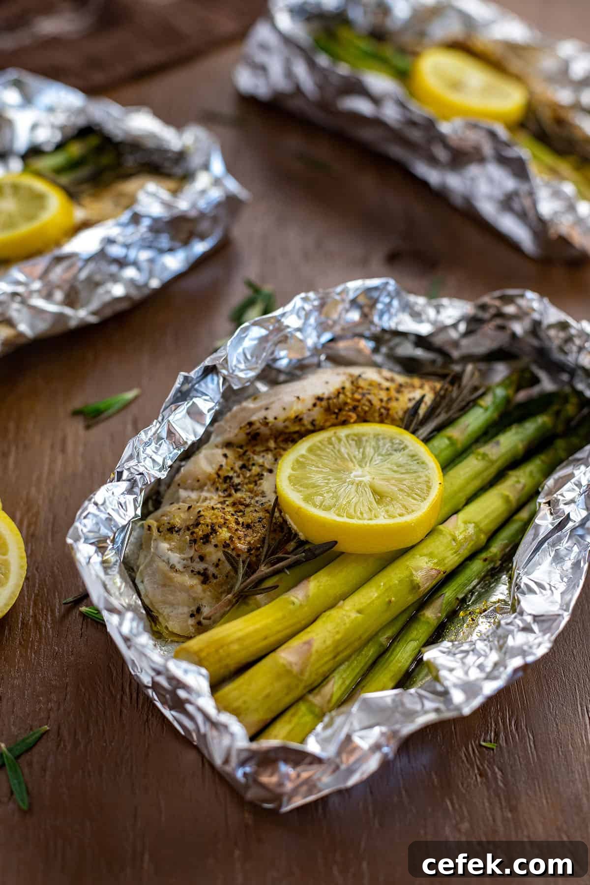 Lemon Pepper Chicken with rosemary and asparagus inside foil packet with lemon slices on top.