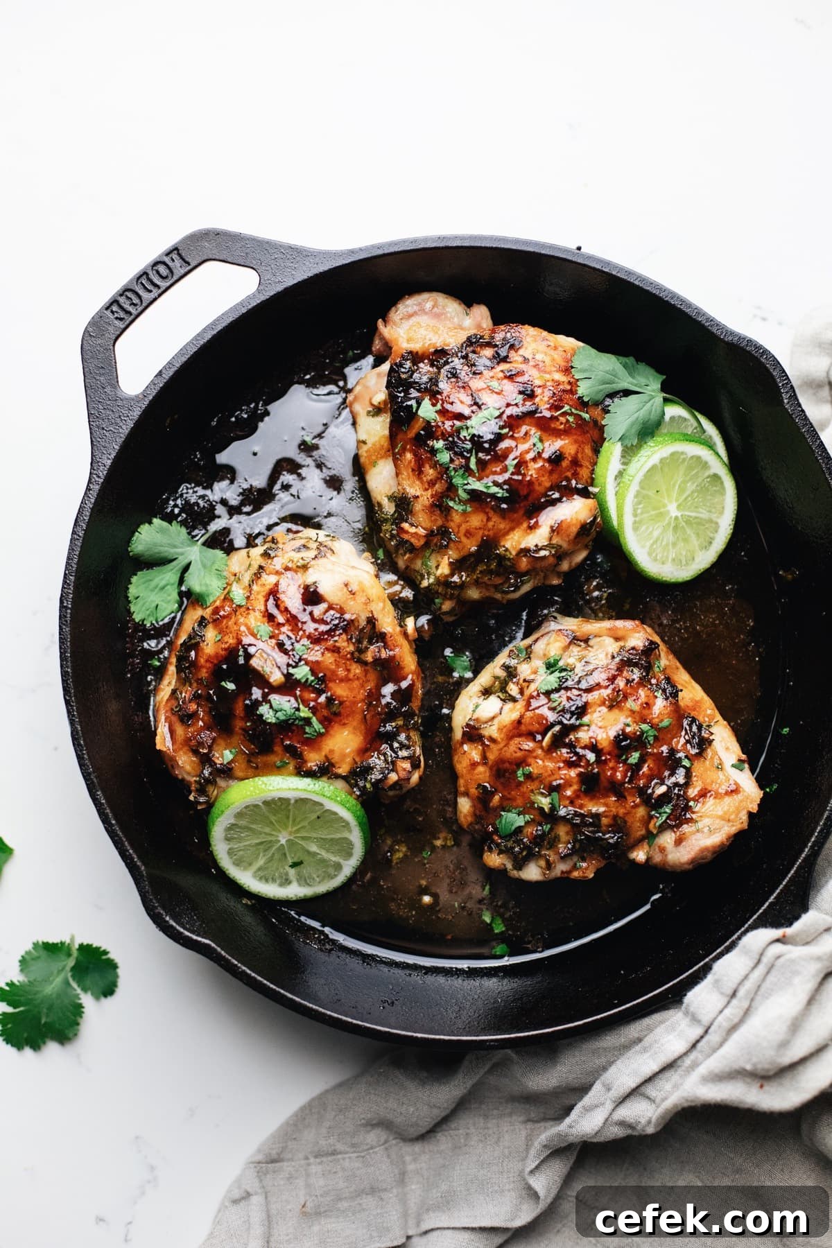 A black cast iron skillet with roasted chicken thighs and lime slices.