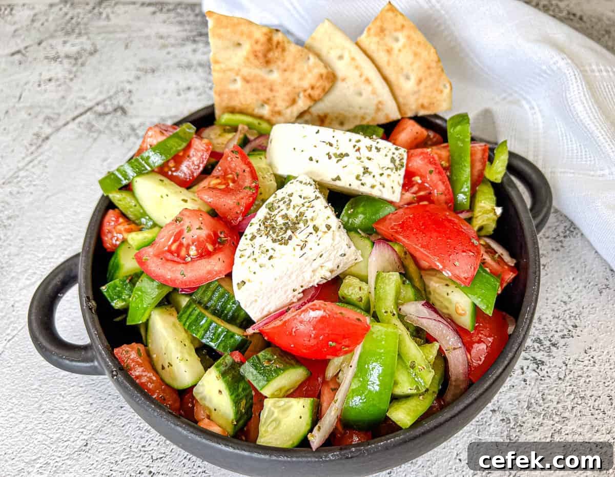 A black bowl contains a Horiatiki salad with blocks of feta cheese, garnished with herbs.