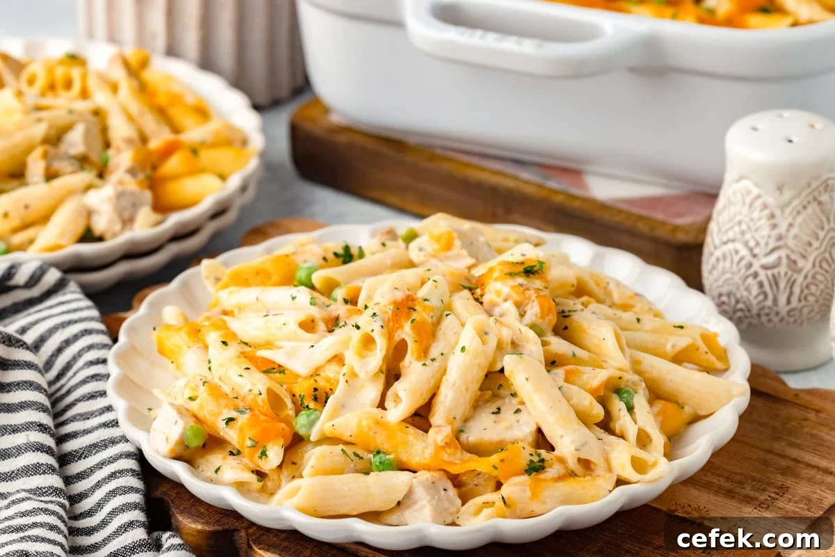 Creamy chicken pasta bake with peas and cheese on a white scalloped plate.