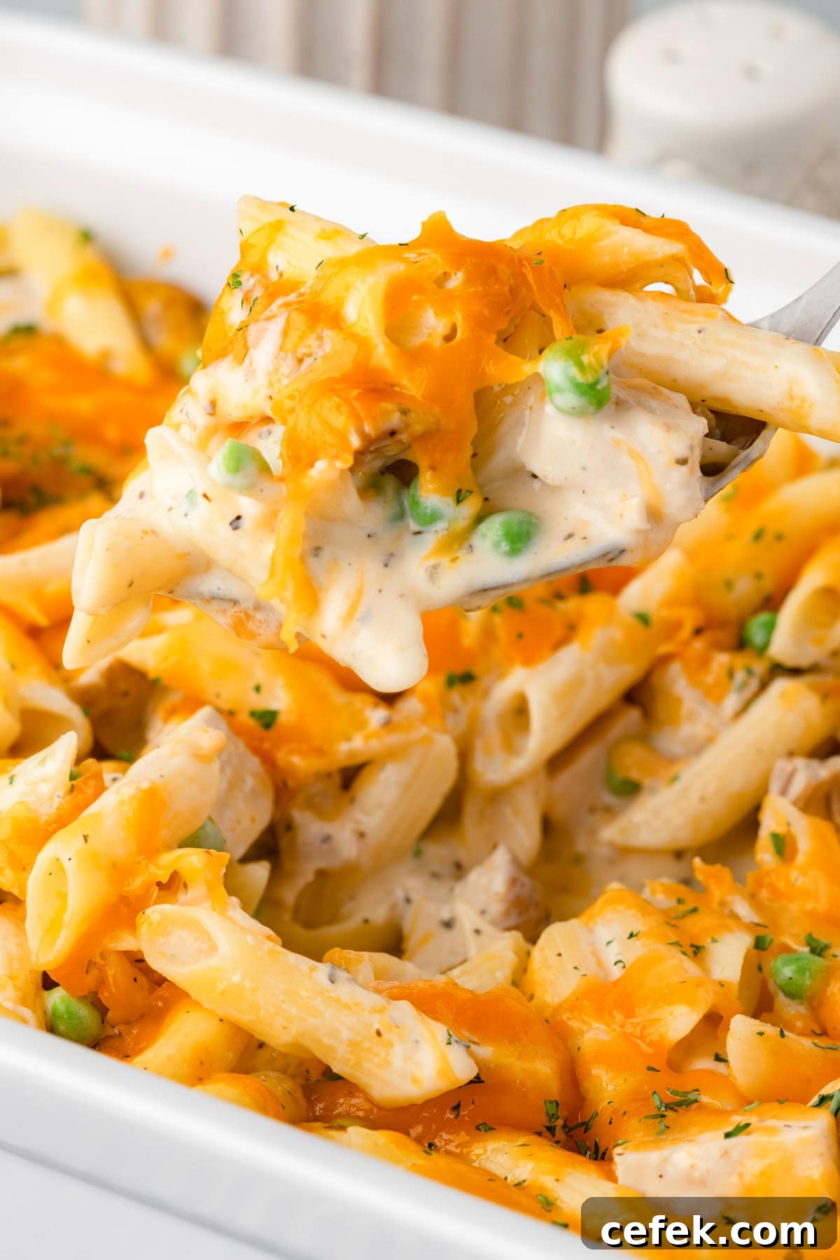 Creamy chicken pasta bake with peas and cheese being scooped from a white casserole dish.