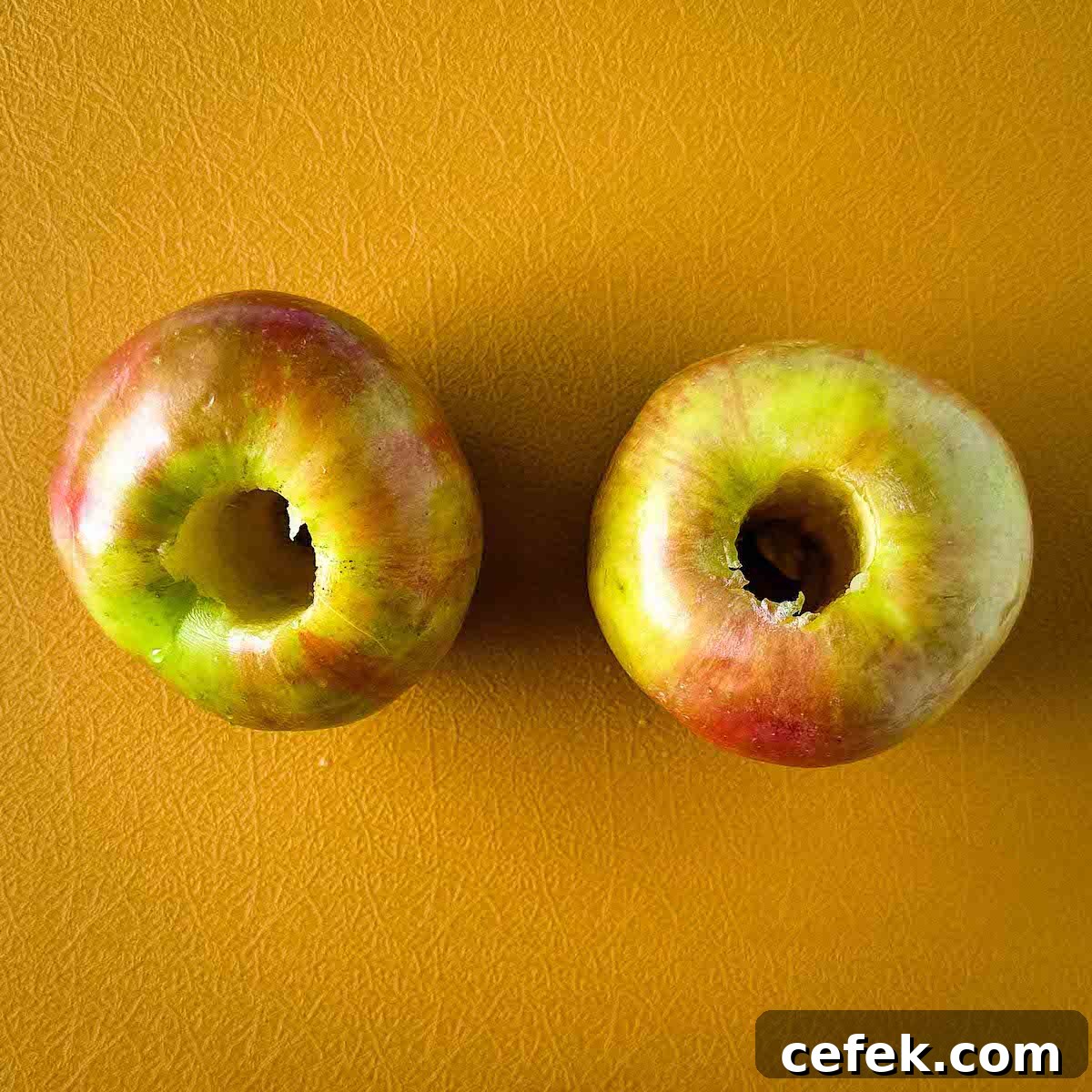 Cored apples sit on a yellow cutting board.