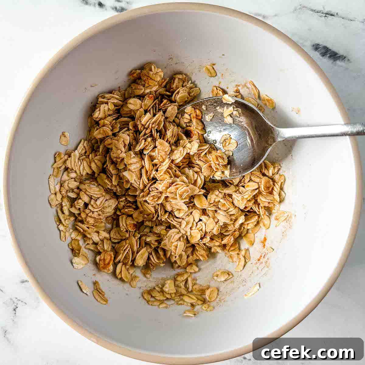 Oats, maple syrup, and cinnamon are mixed together in a white bowl.
