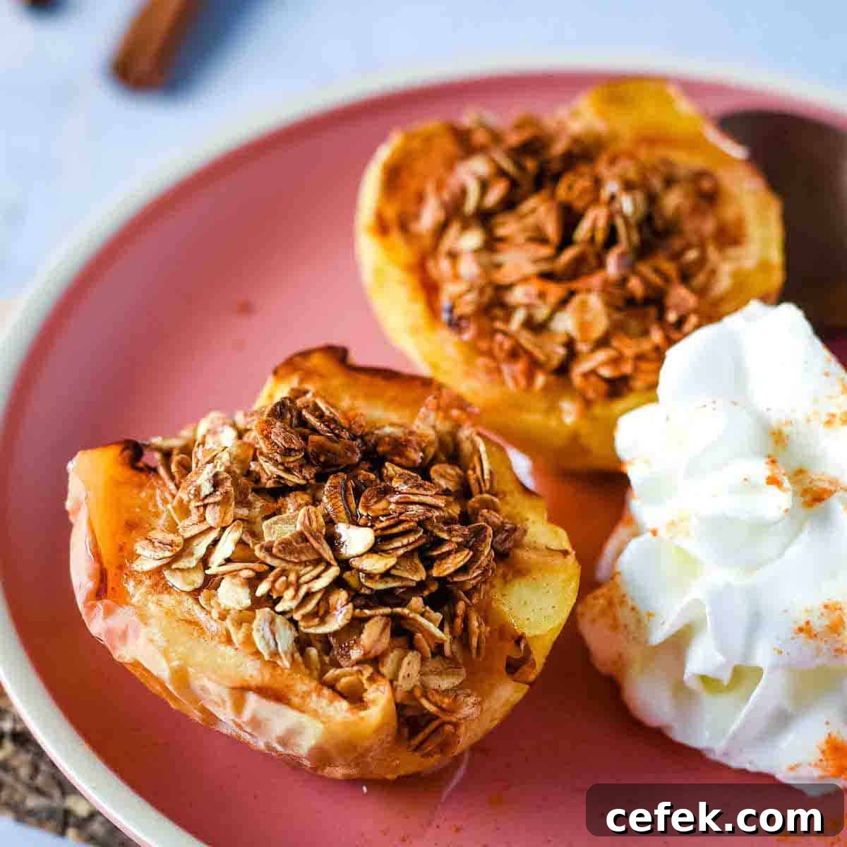 Two baked air fryer apple halves are shown on a pink plate with whipped cream.