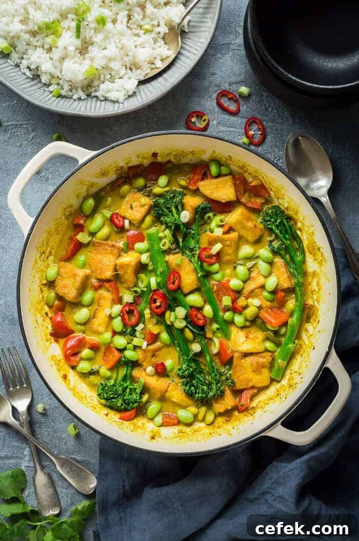 A white cast iron pan full of vegan lemongrass coconut curry with a grey bowlful of rice.