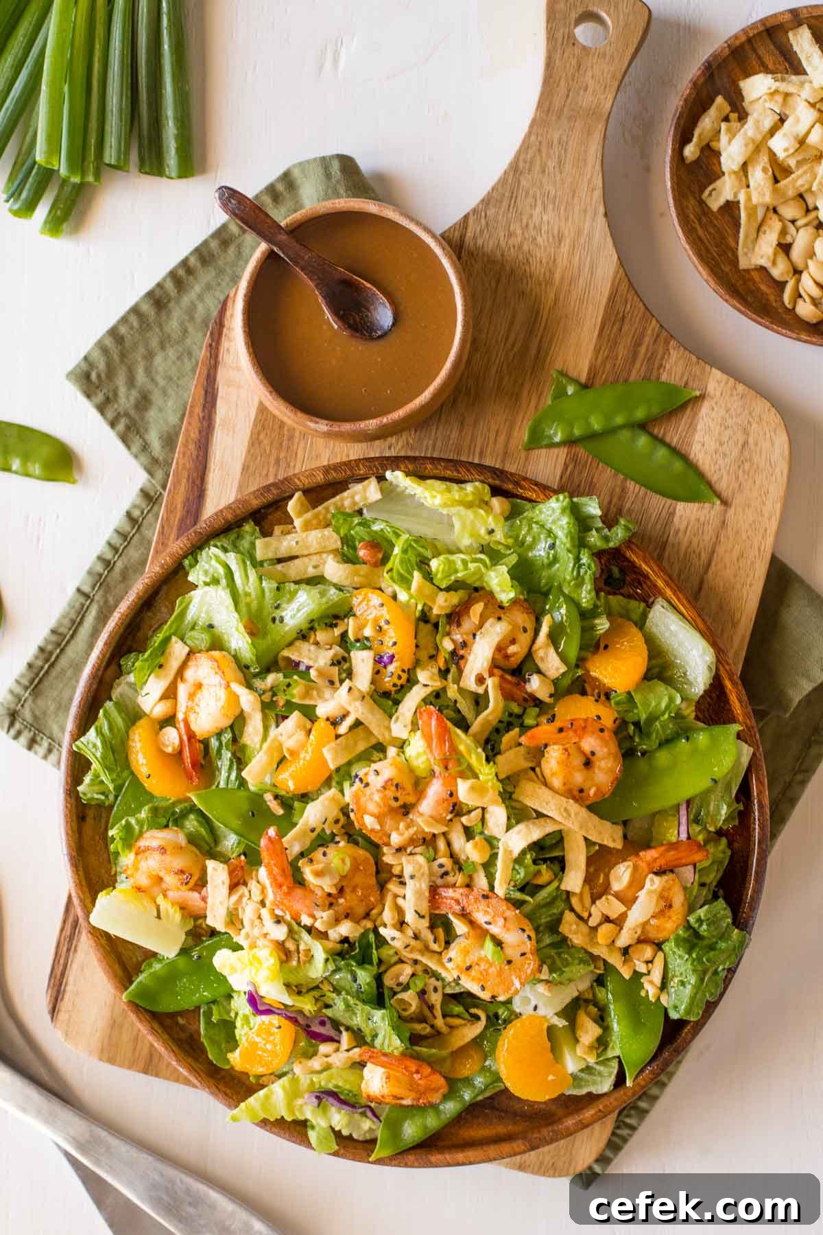 Shrimp Salad on a large serving plate, sitting next to a small wood bowl of the Spicy Peanut Dressing and a bowl of crispy wonton strips and peanuts. 