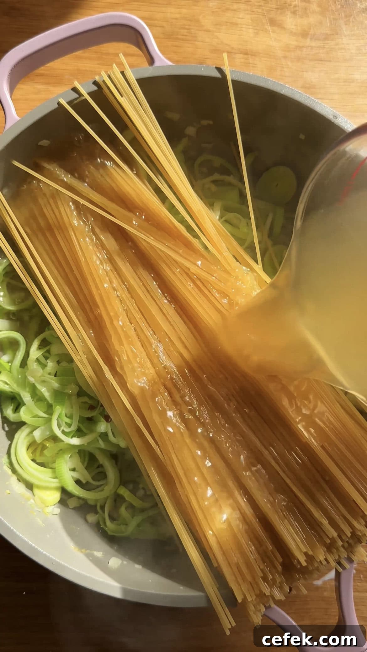 adding stock to pasta in a large saucepan
