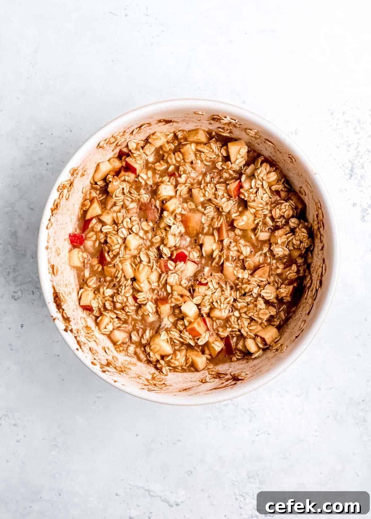 apples, oats, maple syrup, almond milk, apple butter, and other oatmeal ingredients mixed in a white bowl