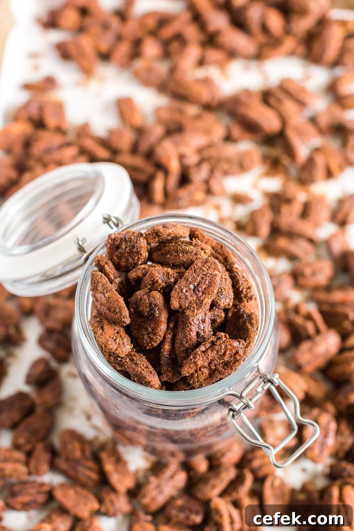 Gingerbread-Spiced Candied Pecans 3 Candied pecans in a glass jar with pecans scattered around.