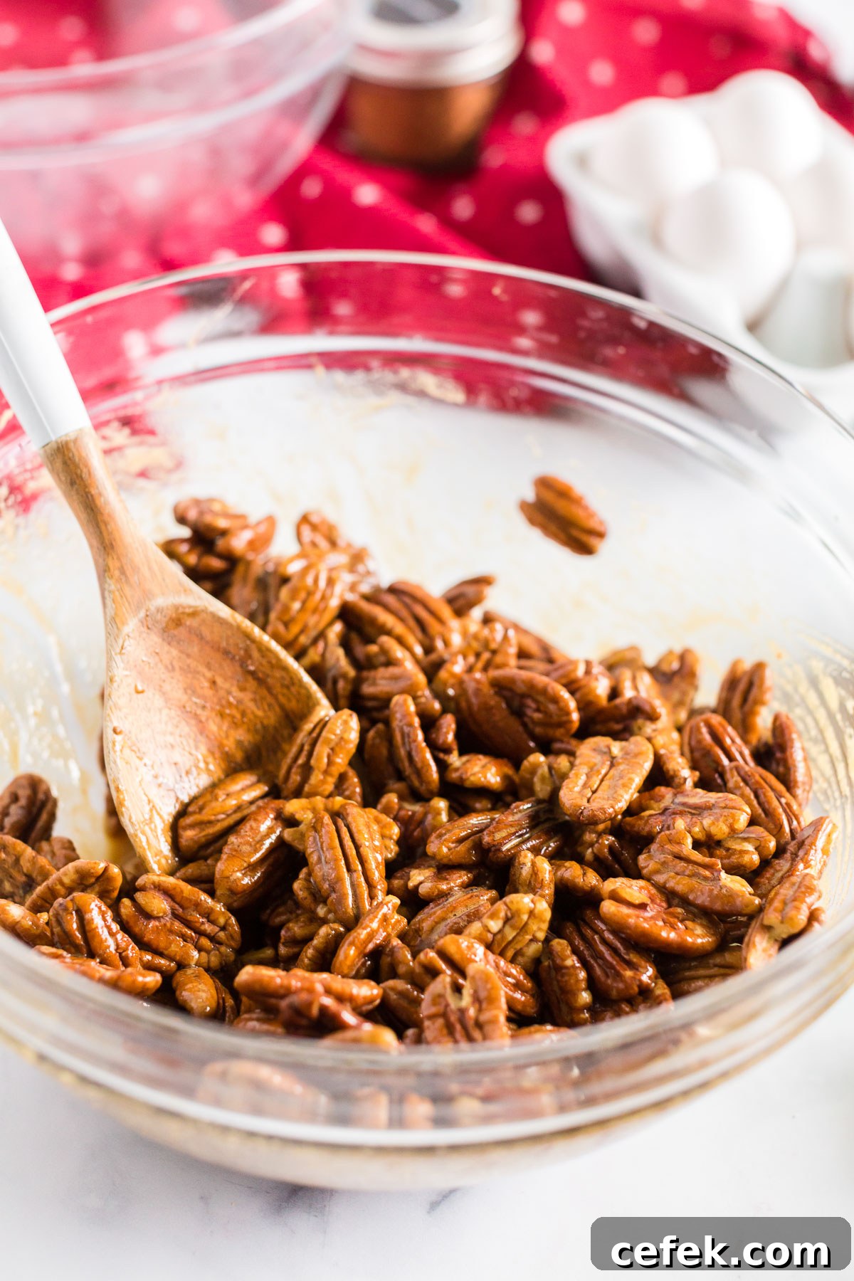 Gingerbread-Spiced Candied Pecans 5 pecans in a mixing bowl with a wooden spoon.