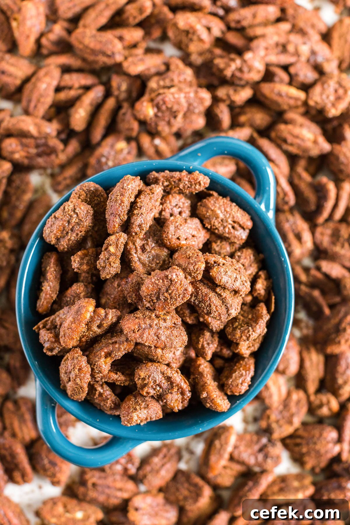 Gingerbread-Spiced Candied Pecans 9 overhead photo of a blue bowl with candied pecans in it and scattered around.