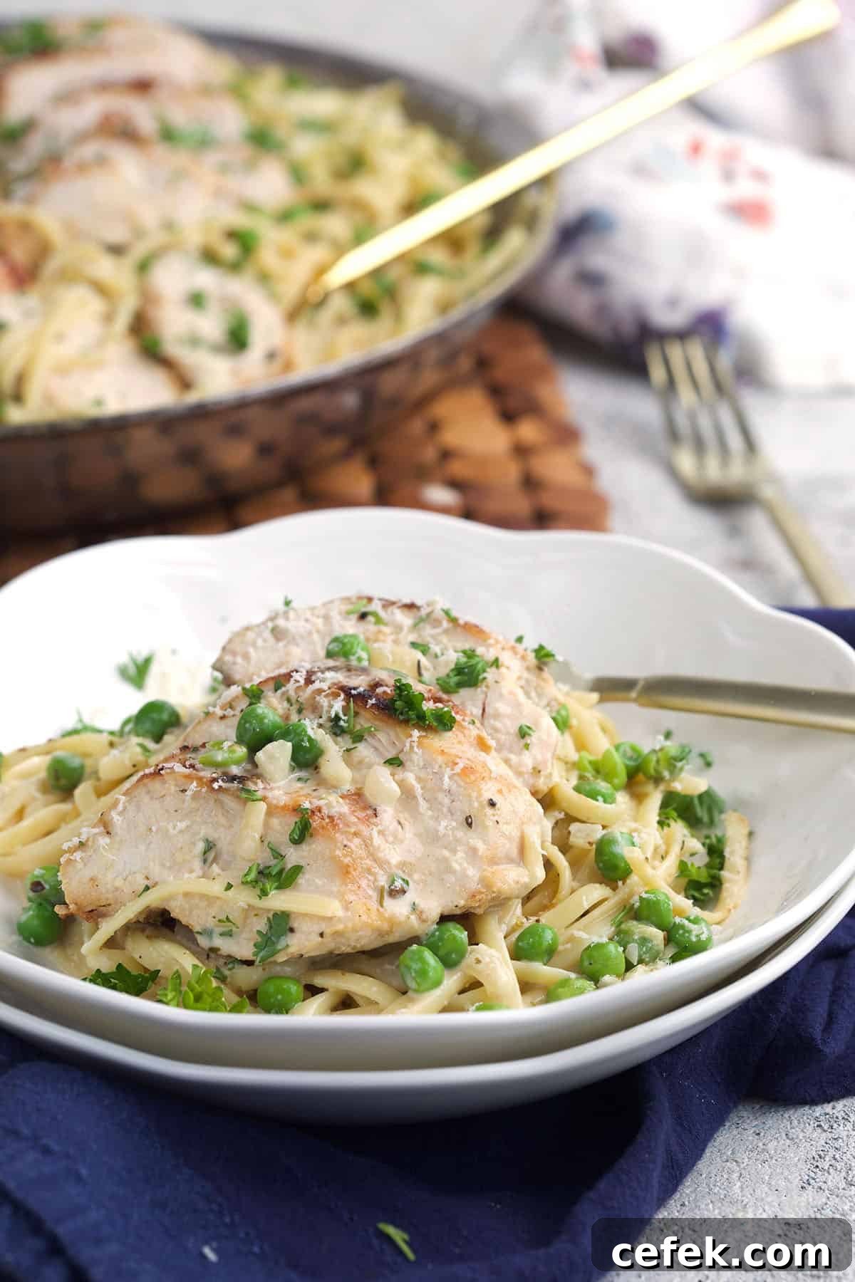 A white plate is topped with a fork and a serving of chicken and pasta. 