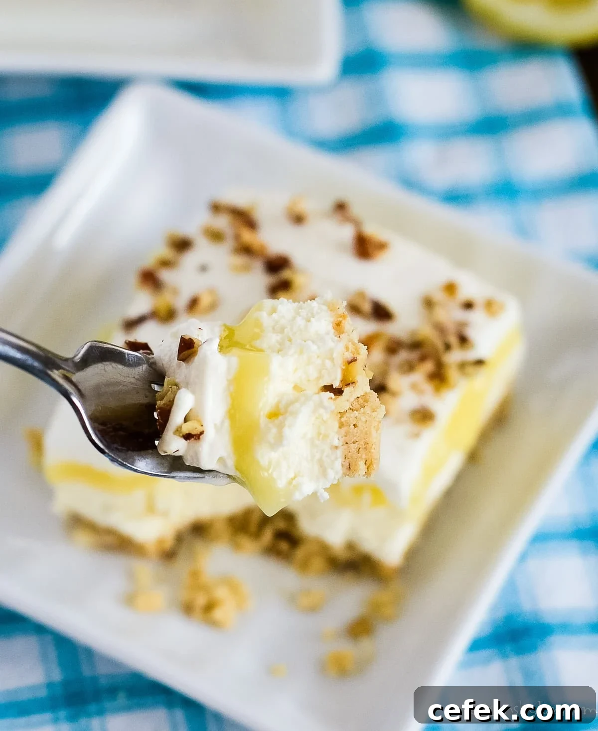 Lemon Lush Dessert Recipe: Creamy Layered Lemon Bars 9 bite of lemon lush on a fork with a plate of dessert underneath
