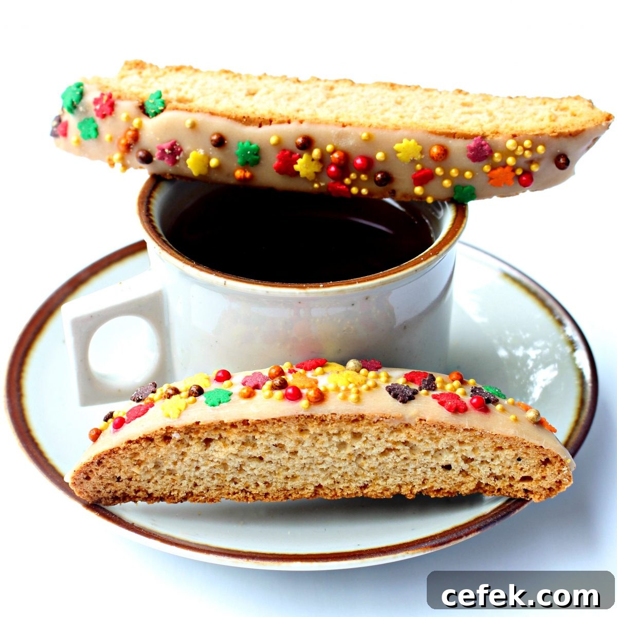 Two biscotti, one on a coffee mug rim and one on the saucer.