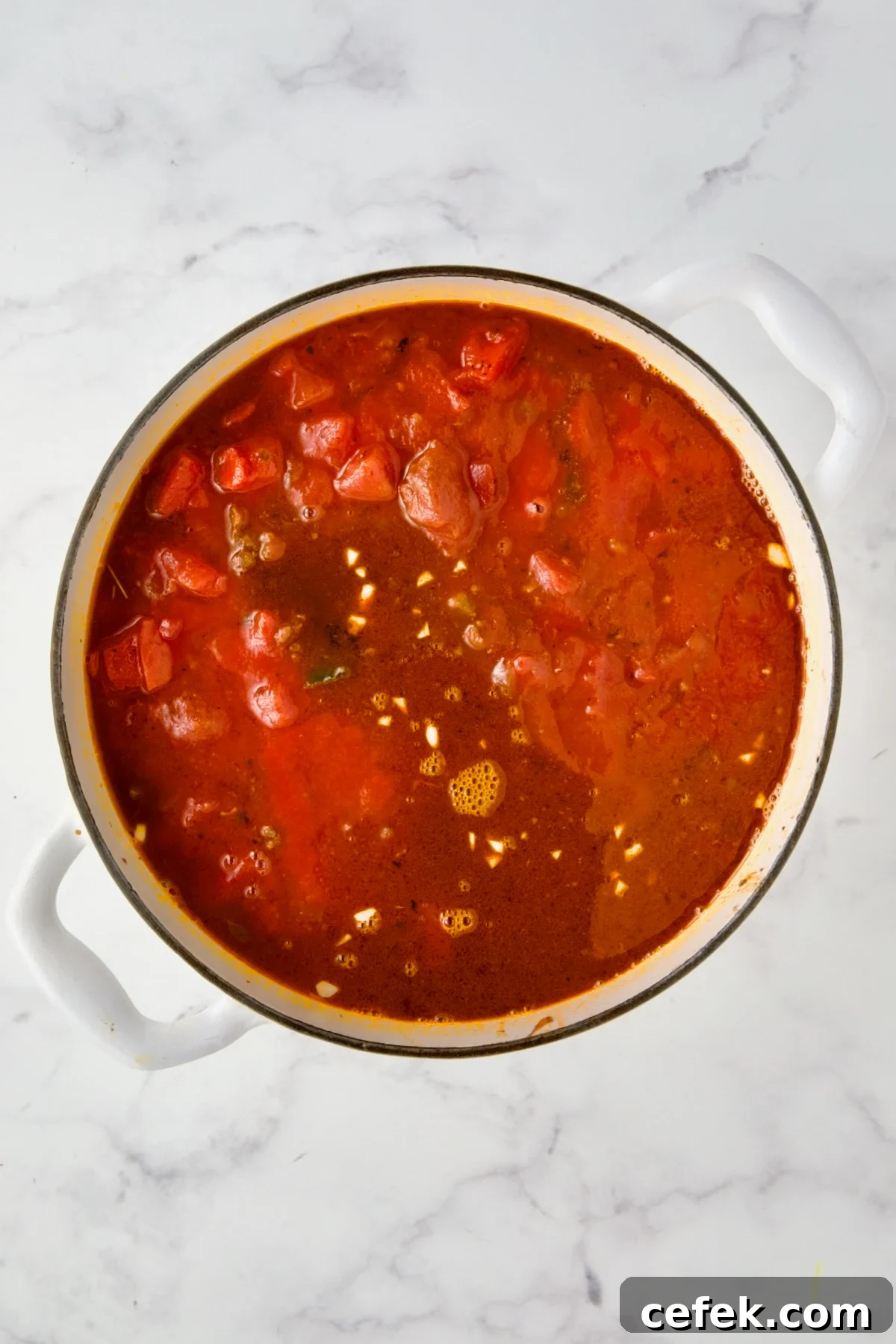 Tomatoes, tomato sauce and beef broth added to white enamel Dutch oven.
