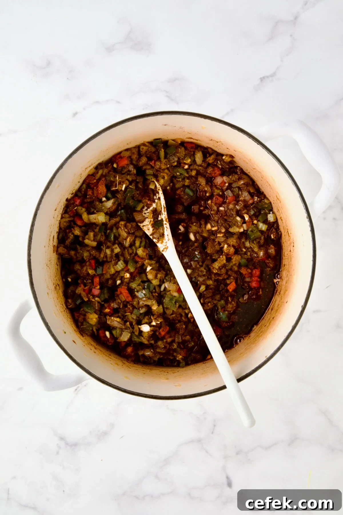 Wine added to spices and vegetables in white enamel Dutch oven.