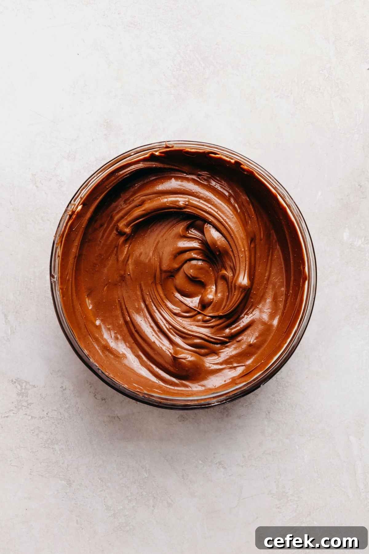 Classic Four-Egg Yellow Sheet Cake with Chocolate Frosting 12 Melted chocolate in a small microwaveable glass bowl on a light grey marbled background.
