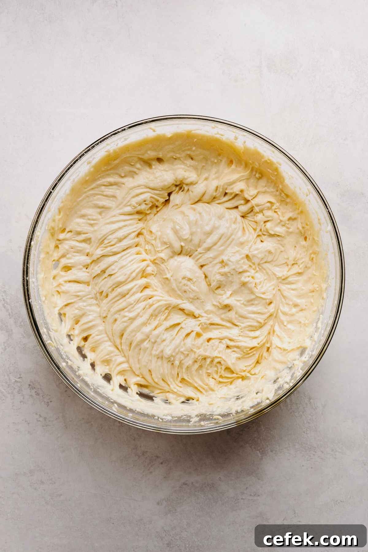 Classic Four-Egg Yellow Sheet Cake with Chocolate Frosting 10 Yellow cake batter in a large glass mixing bowl on a light grey marbled background.