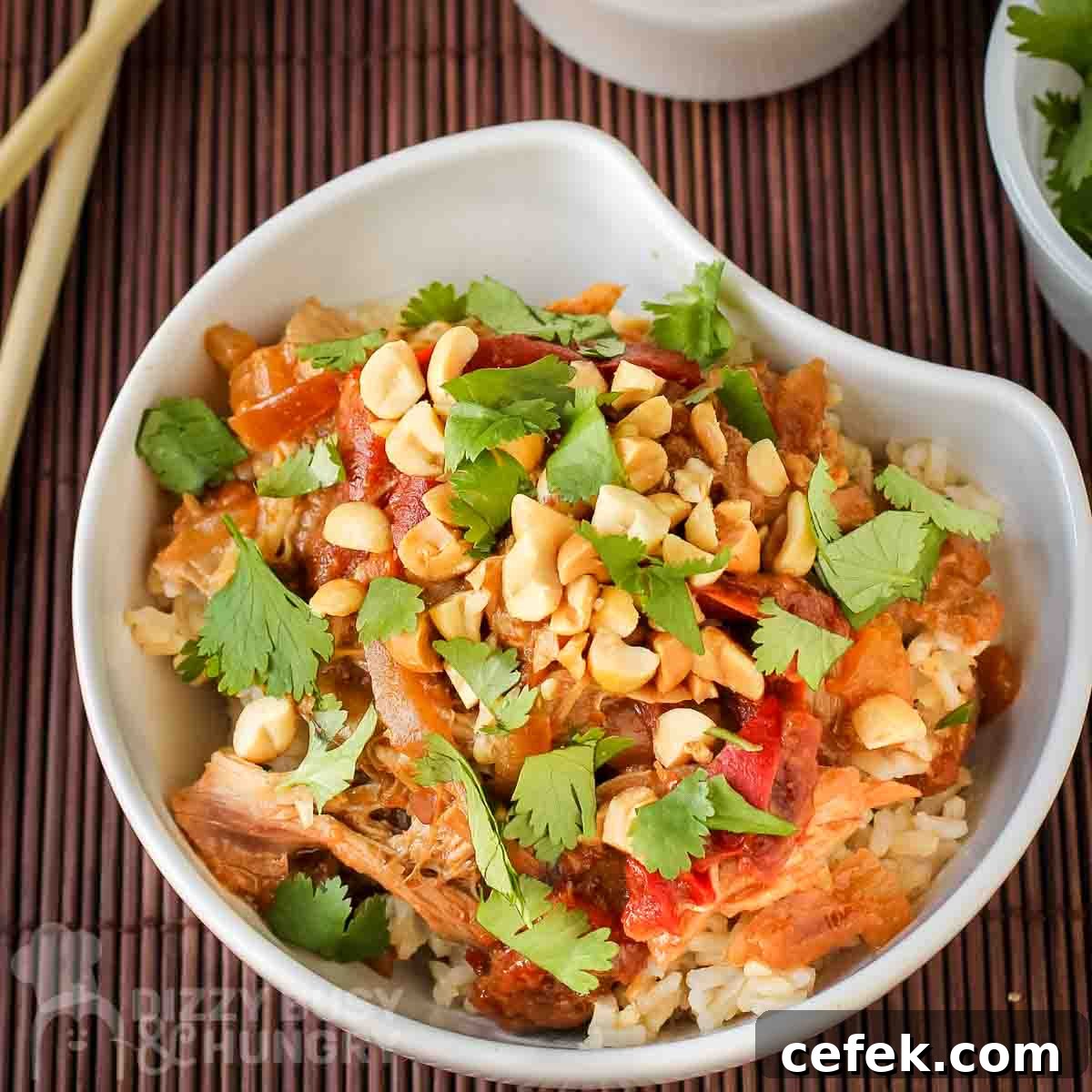 Spicy Slow Cooker Thai Peanut Chicken Recipe 5 Overhead shot of Thai peanut chicken garnished with herbs in a white bowl on a wooden placemat.