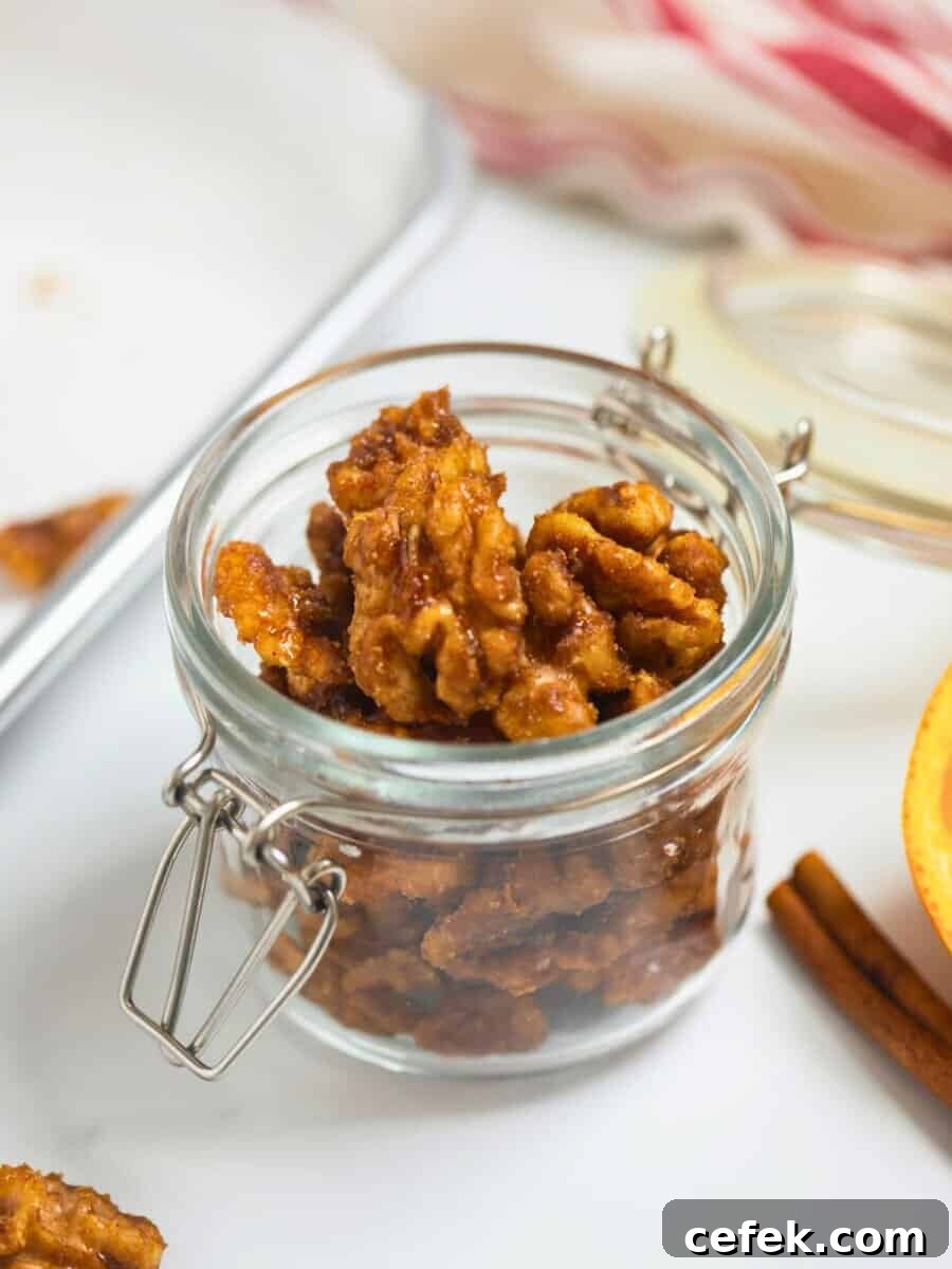 Easy Candied Walnuts Small jar of homemade candied walnuts made with cinnamon, cayenne, and orange next to fresh orange and cinnamon sticks.