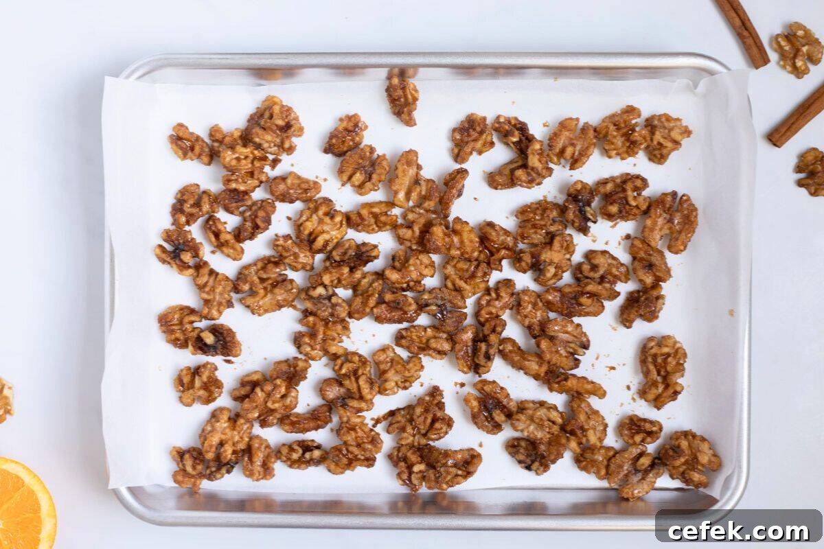 Candied Walnuts with Orange Walnuts coated with caramelized mixture made from orange juice, orange zest, brown sugar, white sugar, cinnamon, salt, and cayenne spread out on parchment paper lined baking sheet.